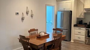 A dining area with a wooden table and chairs, a kitchen with white cabinets, and a door leading outside. - Delightful 1-bedroom poolside house with AC in charming Hahira. (Hahira)