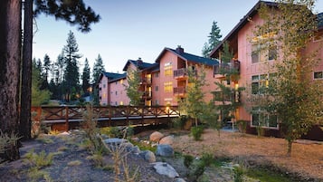A multi-story hotel with balconies, a wooden bridge, and a natural landscape with trees and rocks.
