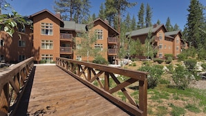 A wooden deck leading to a building with multiple floors and balconies, surrounded by trees. - Lake Tahoe | Alpine Lake Retreat | Pool + Lake (Zephyr Cove)