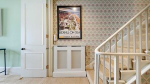A staircase with a white railing, a framed poster of Bexhill-on-Sea, and a white door with a small table beside it. - Gorgeous 3 Bedroom Flat - Pimlico (London)
