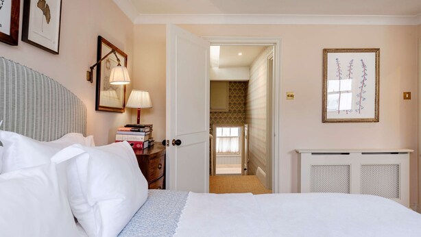 A bedroom with a bed, bedside table, lamp, framed pictures, and a radiator. - Gorgeous 3 Bedroom Flat - Pimlico (London)
