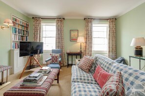 A living room with a sofa, armchair, ottoman, bookshelf, television, and a lamp. - Gorgeous 3 Bedroom Flat - Pimlico (London)