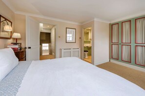 A bedroom with a bed, a dresser, a lamp, a framed picture, a door leading to a bathroom, and a wardrobe with curtains. - Gorgeous 3 Bedroom Flat - Pimlico (London)
