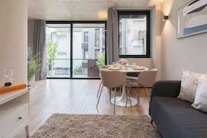 Ein modernes Wohnzimmer mit Essbereich, einer Couch, einem Couchtisch und Blick auf die Stadt durch große Fenster.
