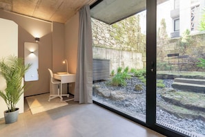Ein modernes Zimmer mit Glastür zu einem Garten, einem weißen Schreibtisch und einer Topfpflanze.