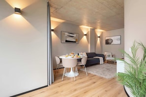 Ein modernes Wohnzimmer mit Essbereich, mit Holzboden, einer Couch, einem Esstisch mit Stühlen und Wandleuchten.