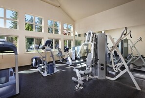 A gym with various exercise machines, large windows, and a high ceiling.