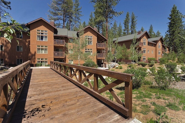 A wooden deck leading to a building with multiple floors and balconies, surrounded by trees.