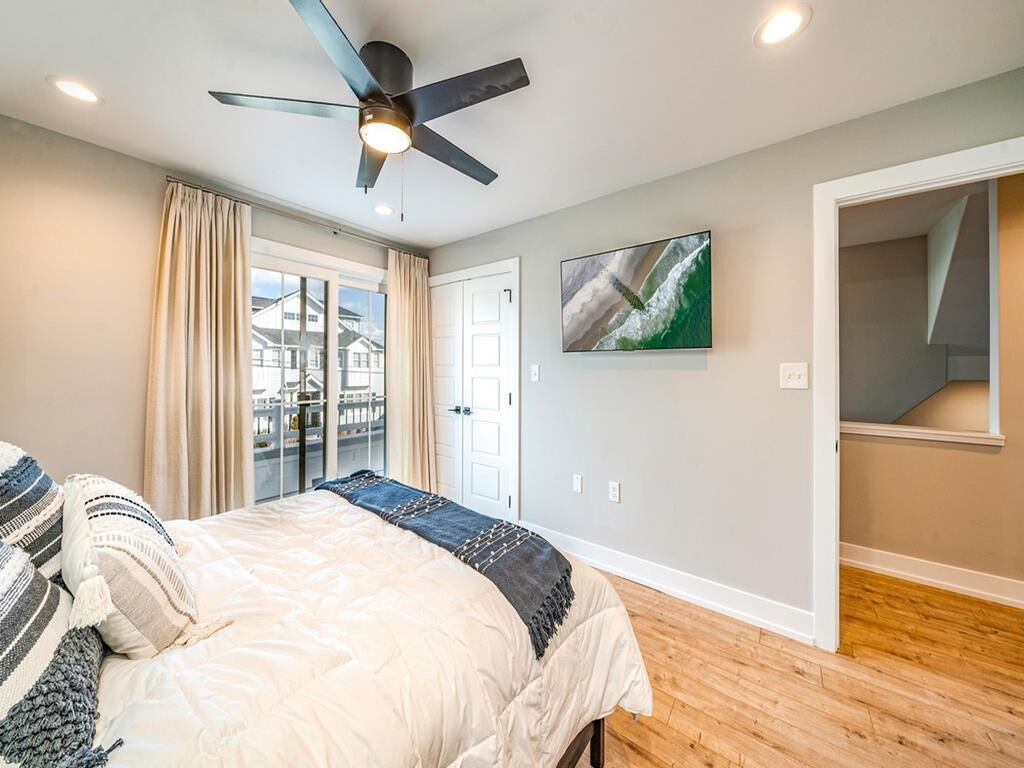 A bedroom with a bed, a ceiling fan, a window with curtains, a door, and a painting on the wall.