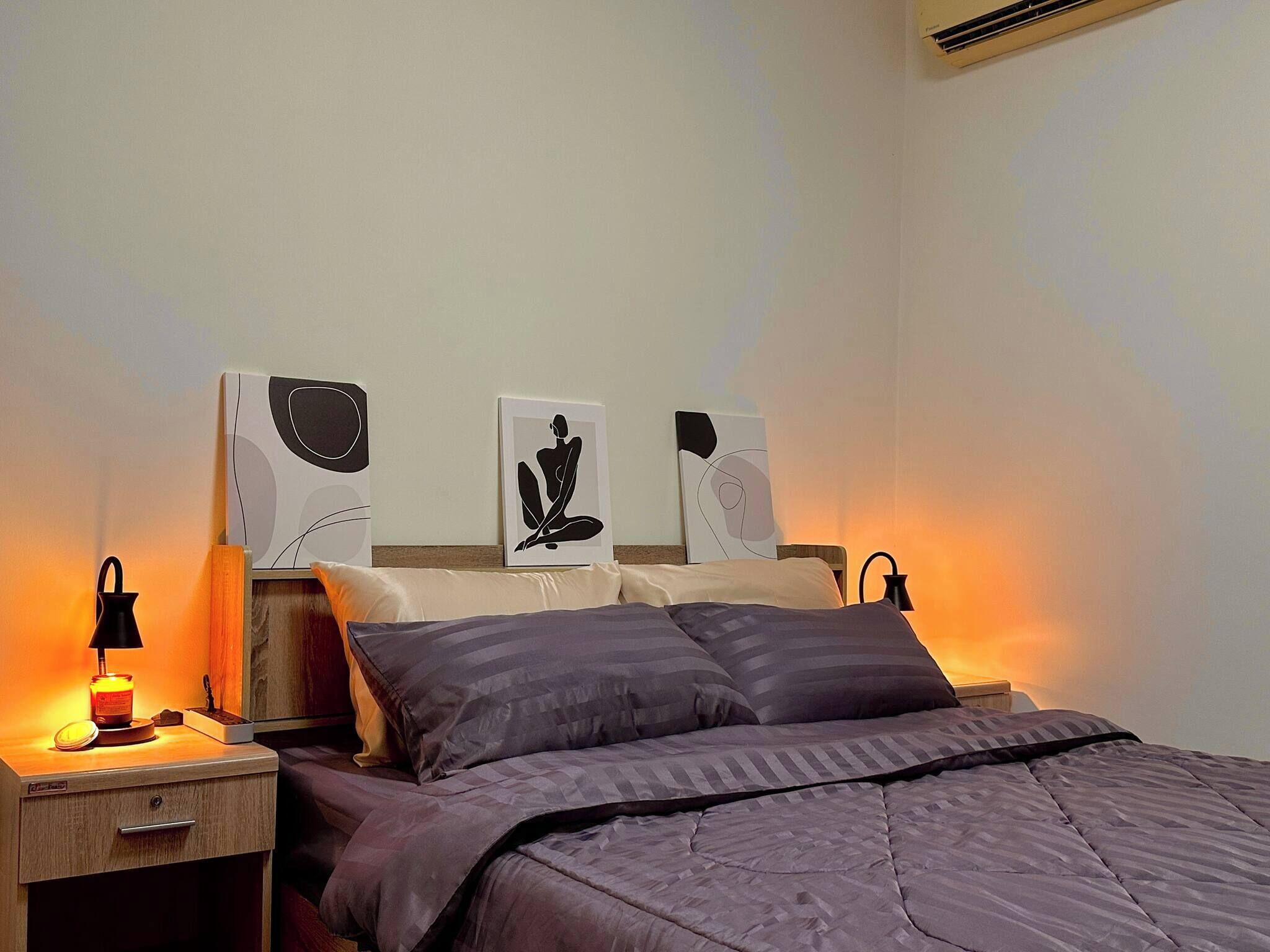 A neatly made bed with a dark-colored comforter and pillows, a bedside table with a lamp, and three wall-mounted artworks above the bed.