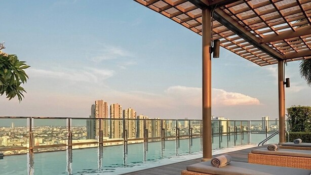 A rooftop pool with a glass barrier, lounge chairs, and a view of a cityscape. - Modern Luxury Escape BTS Udom Suk 0m (Bangkok)
