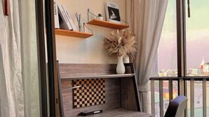 A modern room with a wooden desk, a chessboard, and a view of the city through large windows. - Modern Luxury Escape BTS Udom Suk 0m (Bangkok)
