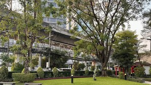 A park with benches, trees, and a building with a modern design. - Modern Luxury Escape BTS Udom Suk 0m (Bangkok)
