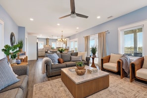 A modern living room with a sofa, armchairs, a coffee table, and a kitchen in the background. - Private Ft. Morgan Retreat / Sleeps 16 / Golf Cart (Gulf Shores)