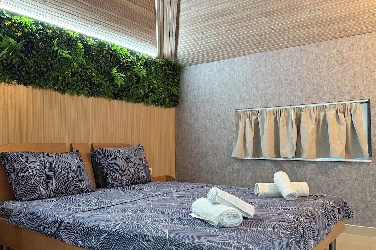A modern hotel room with a bed, a wall-mounted mirror, and a green plant wall.