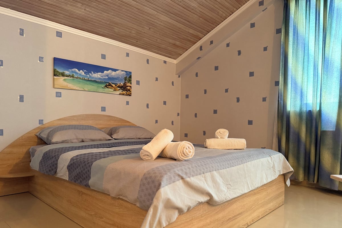 A bedroom with a wooden bed, a painting of a beach scene, and a patterned wall.