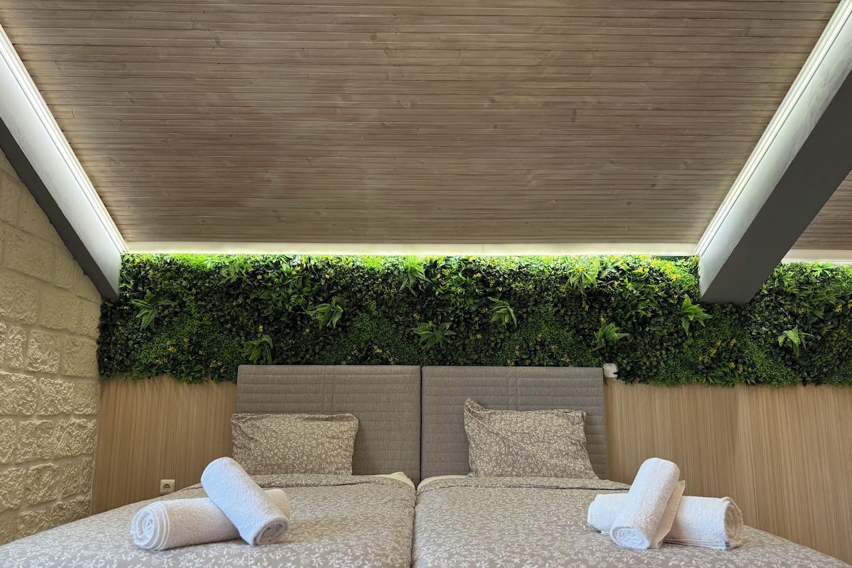 A double bed with a headboard, two pillows, and rolled towels.