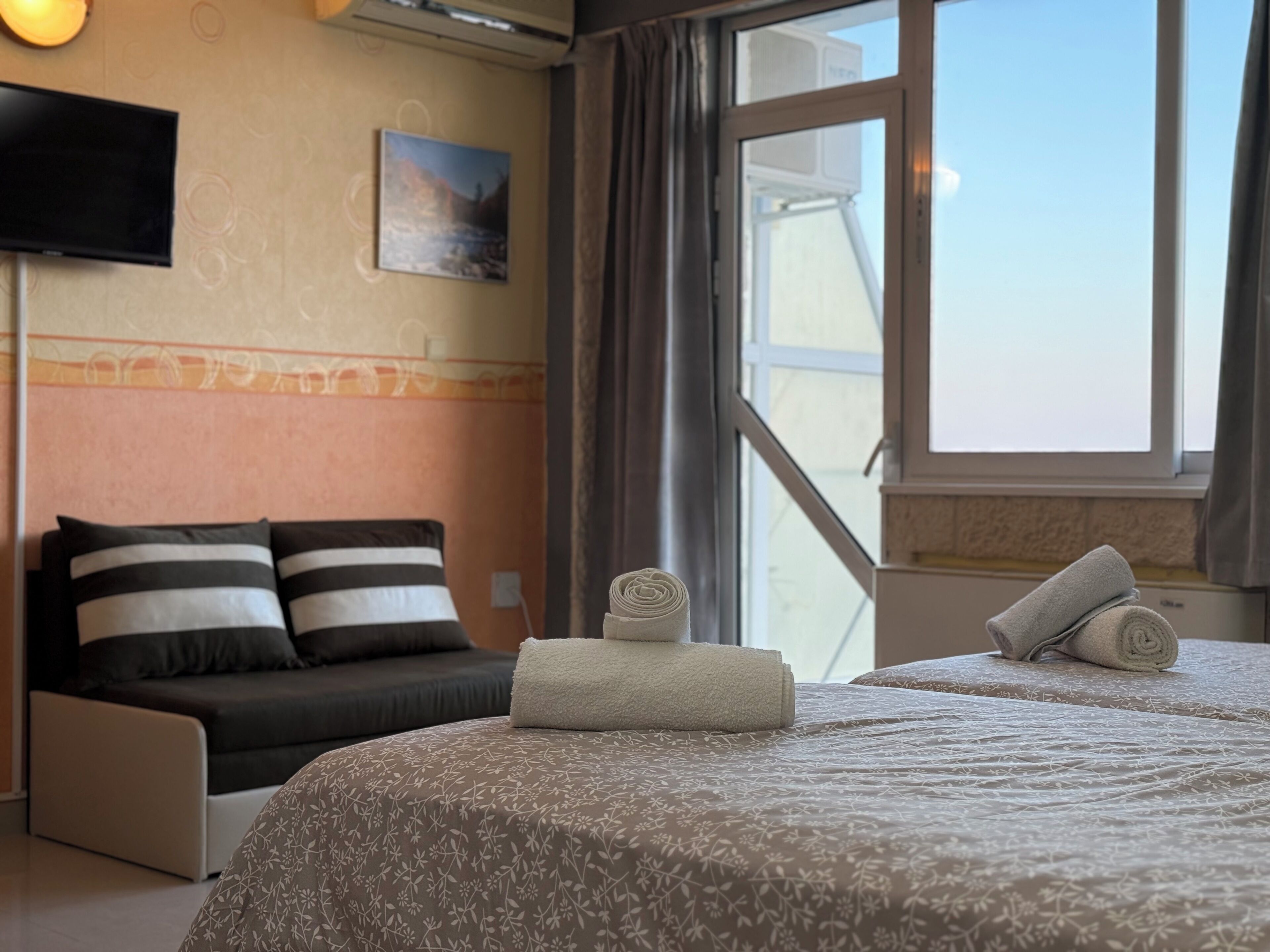 A hotel room with a bed, a sofa, a TV, a painting, and a window with curtains.