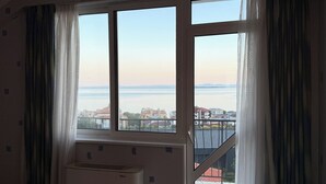 A room with a large window, a radiator, and a view of a body of water and buildings. - Vista Mare Sveti Vlas (Sveti Vlas)