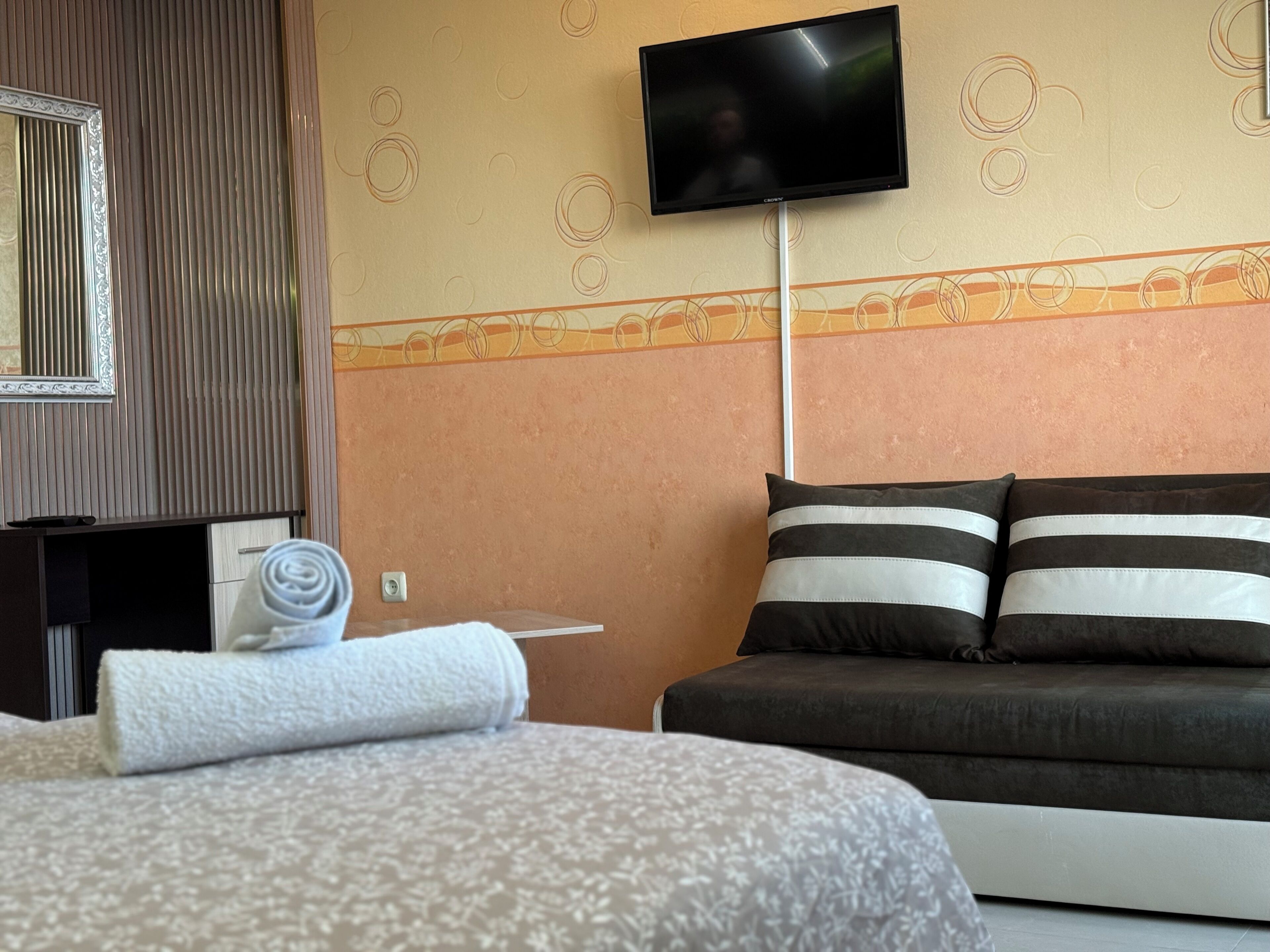 Ein Hotelzimmer mit einem Bett, einem an der Wand montierten Fernseher, einem kleinen Tisch und einem Spiegel.
