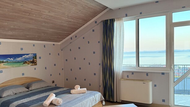 A bedroom with a bed, a view of the sea, a painting on the wall, and a window with curtains. - Vista Mare Sveti Vlas (Sveti Vlas)