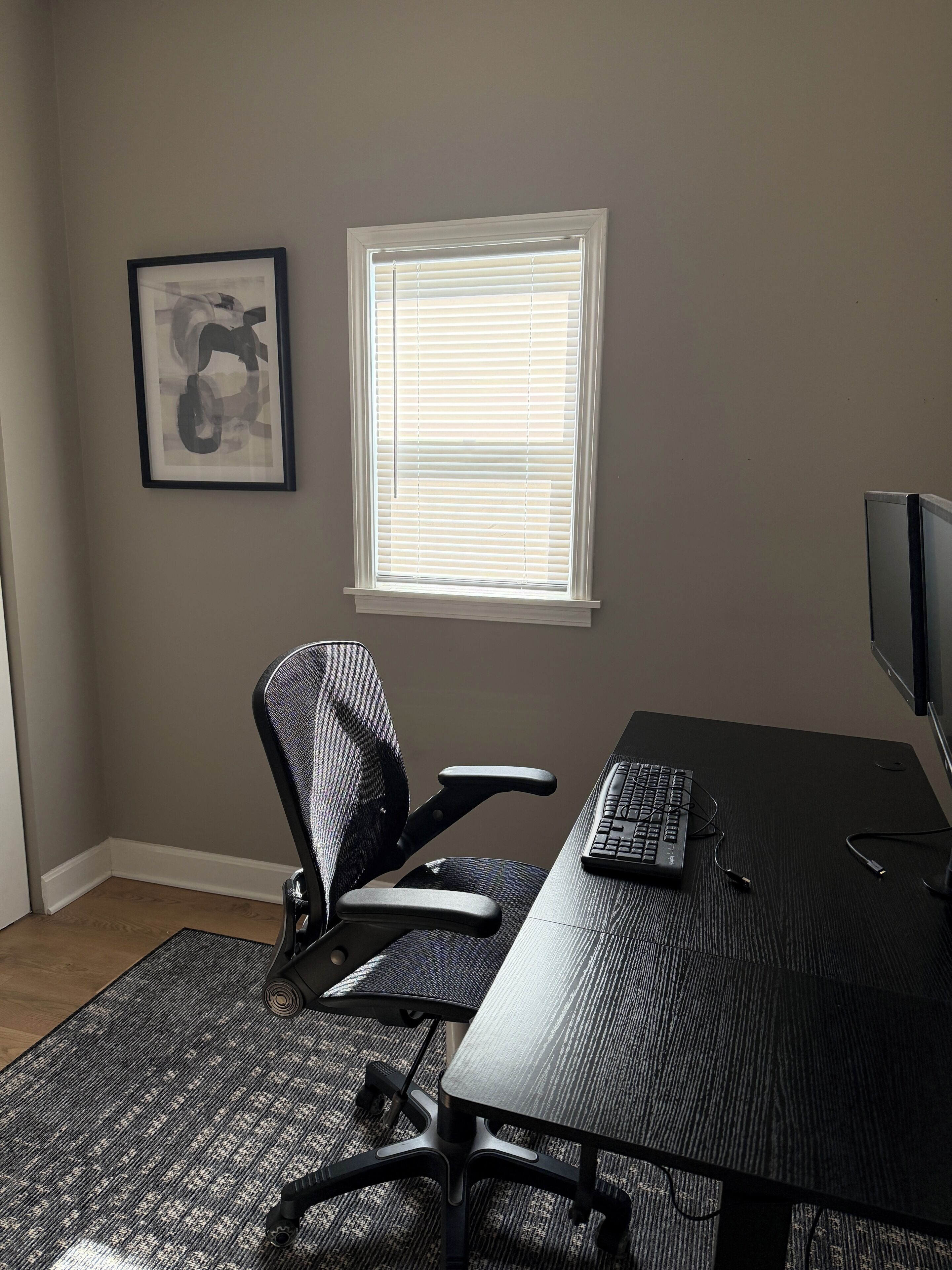 Una habitación con escritorio, silla, computadora y ventana con persianas.