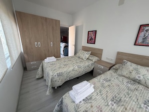 Een slaapkamer met twee bedden, een houten garderobe en een deur naar een andere kamer.