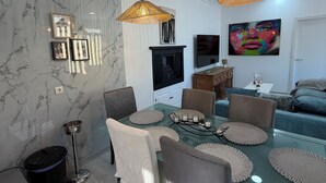Un espace de salle à manger moderne avec une table en verre, des chaises en osier et des luminaires suspendus.