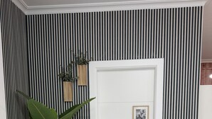Une pièce avec un papier peint à rayures, une porte blanche, un tableau encadré et une plante en pot.