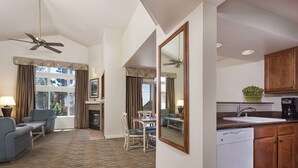 A hotel room with a living area, dining table, chairs, a fireplace, a kitchen with a sink and cabinets, and a ceiling fan.