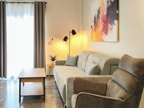 A living room with a sofa, a small table, a floor lamp, and a painting on the wall. - Casa Libero - Steps to Old Town & Venetian Harbor (Chania)