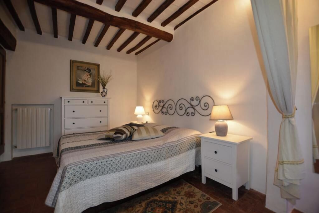 A bedroom with a bed, bedside tables, a radiator, a wall-mounted picture, and a decorative headboard.