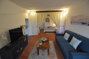 A living room with a TV, sofa, and a bed with curtains. - Panoramic apartment in medieval village (Radicondoli)