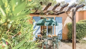 Un patio con mesa y sillas, una pérgola y un edificio con contraventanas azules.