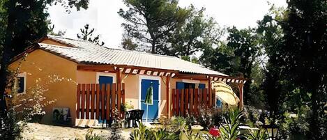 A single-story building with a corrugated metal roof, a blue door, and a small porch area with a chair.