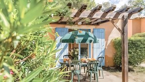 Eine Terrasse mit Tisch und Stühlen, einer Pergola und einem Gebäude mit blauen Fensterläden.