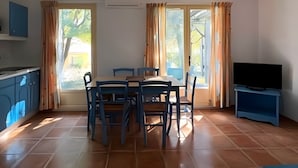 Een eethoek met een tafel en stoelen, een televisie en een keuken met kasten.