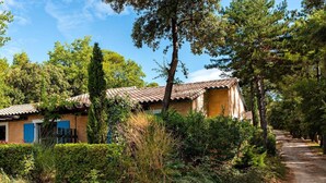 Et rustikt hus med tegltag, omgivet af frodig vegetation og en grussti.