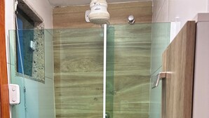 Et brusehjørne med glasvægge, en trævæg, et hvidt brusehoved og en hylde med toiletartikler.