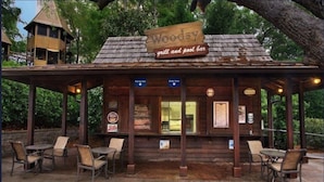 En rustik träbyggnad med skylten ”Woody grill och poolbar”, med utomhusplats och en täckt uteplats.