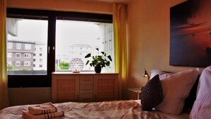 Et hotelværelse med en seng, et vindue med gardiner, en potteplante, en lampe og et billede på væggen.