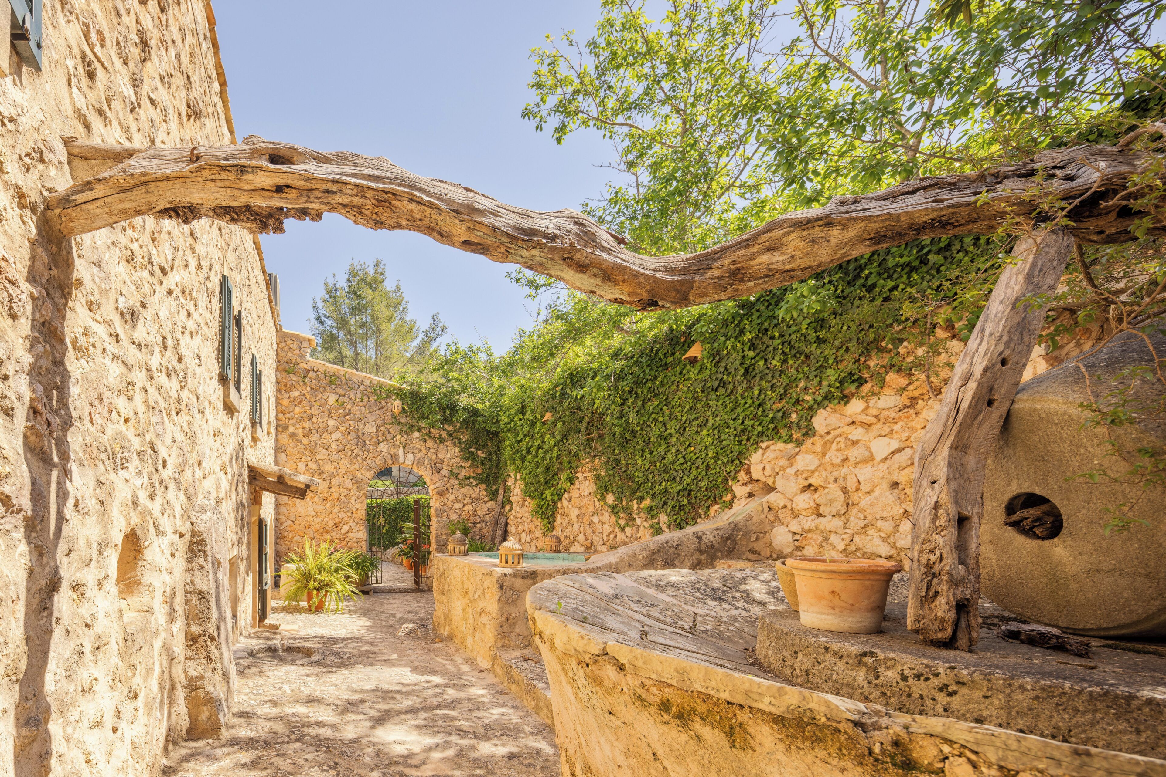 A stone building with a rustic wooden archway, potted plants, and a stone wall with greenery.