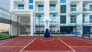 An indoor basketball court with a blue basketball hoop, surrounded by a fence, and a building with multiple windows in the background. - Free Housekeeping Visits During Your Stay - Stayshort - Modern New Studio in Arjan That Sleeps 4 (Dubai)