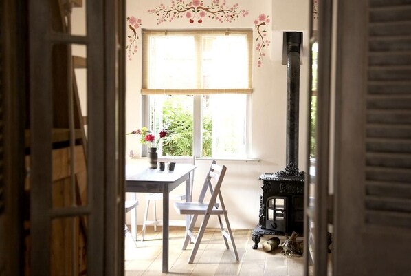 Ein Zimmer mit Tisch, Stühlen, einem Fenster mit Jalousien, einer Wand mit Dekoration und einem Kamin.