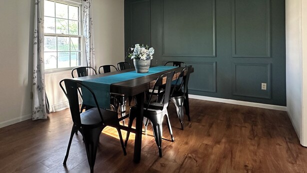 Un comedor con una mesa y sillas de madera, una planta en maceta y una ventana con cortinas.