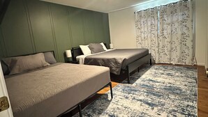 Una habitación con dos camas, una pared verde de acento, un tapete estampado y una ventana con cortinas florales.