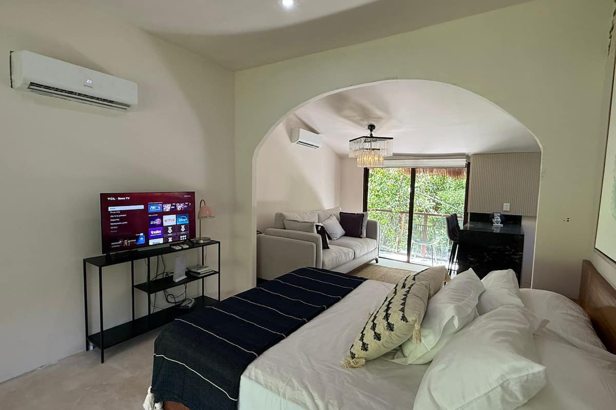 A bedroom with a bed, a TV, a desk, and a balcony with a view.