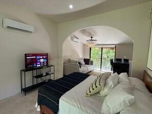 A bedroom with a bed, a TV, a desk, and a balcony with a view. - Casa Florentina (Tulum)