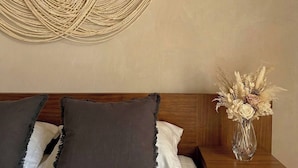 A bed with two pillows, a wooden headboard, a wall-mounted macrame piece, and a bedside table with a vase of dried flowers. - Casa Florentina (Tulum)
