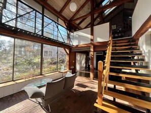 Una habitació àmplia amb grans finestres, una escala de fusta i una zona de seients amb una taula de vidre.